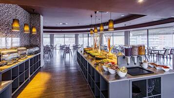 A modern buffet setup with various food stations and seating areas, large windows offering views of the city, and contemporary lighting fixtures.