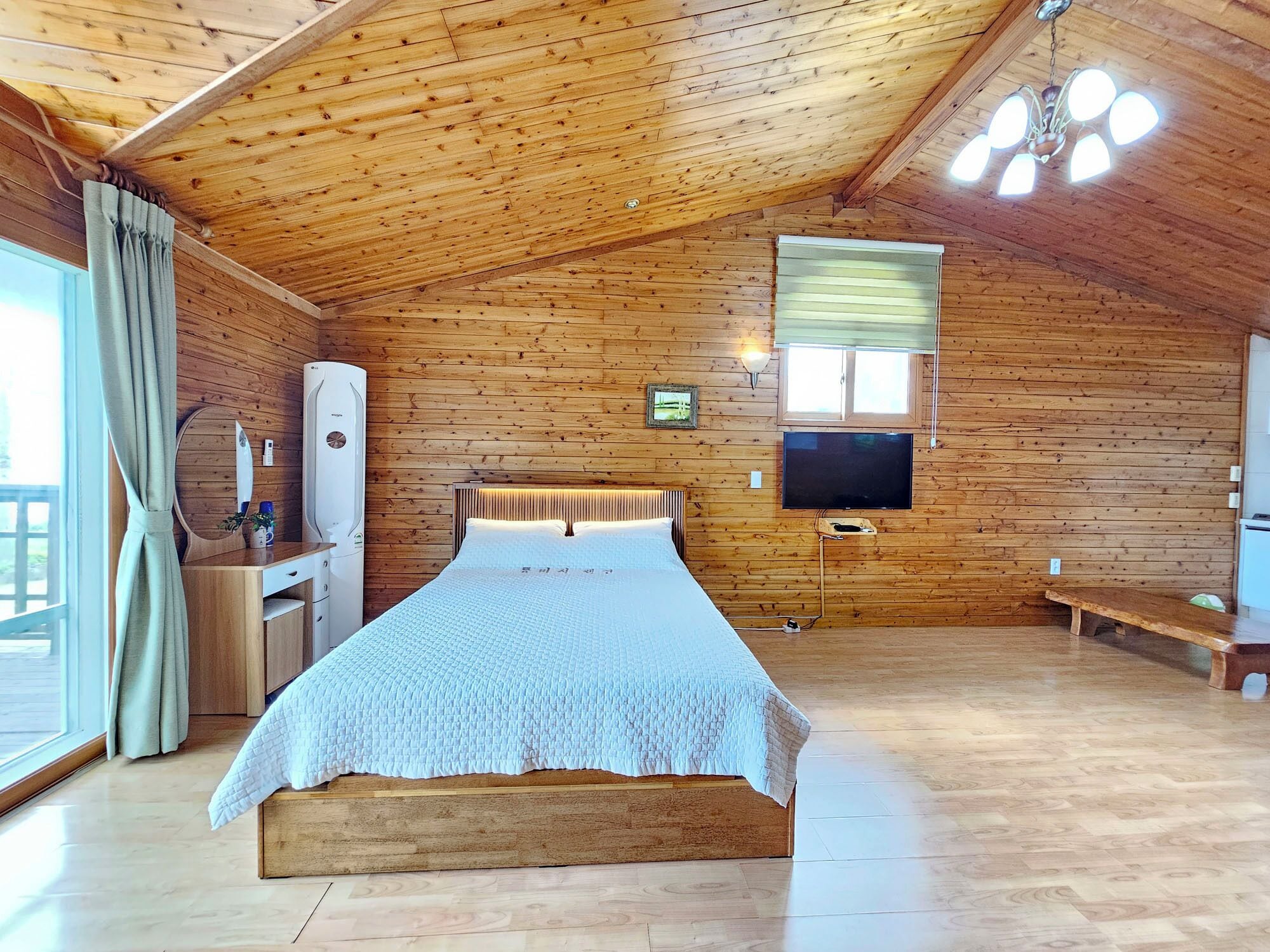 A wooden cabin bedroom with a bed, a TV, a window, and a wooden ceiling.