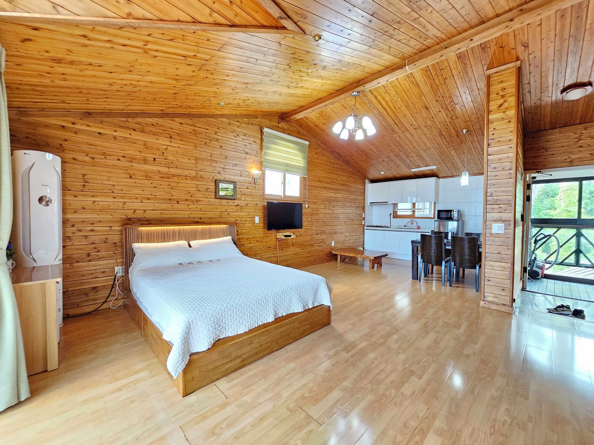 L’intérieur d’une cabane en bois, avec un lit, un coin cuisine et une grande fenêtre.
