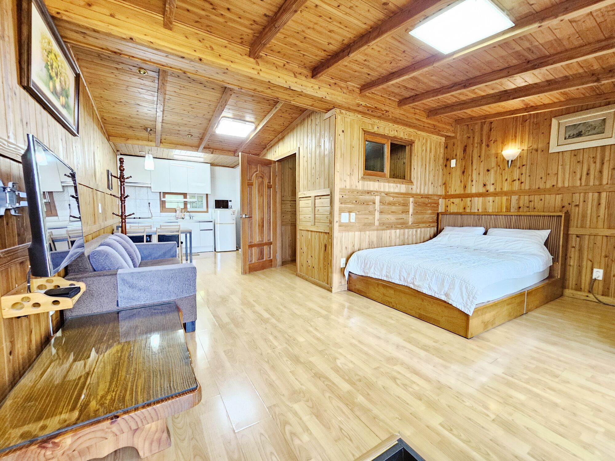 A wooden interior with a bed, a sofa, a table, and a kitchen area.