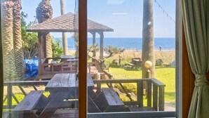 Ett trädäck med picknickbord och en pergola med utsikt över en strand.