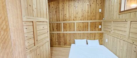 A wooden-paneled room with a bed, a window, and a ceiling light.