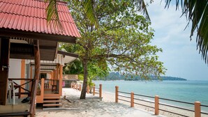 A beachfront property with a red-roofed building, a palm tree, and a sandy beach with a railing. - Lamai Resort (Koh Samui)