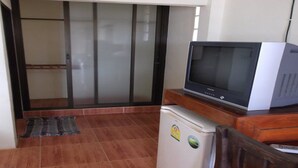 A compact living space with a sliding glass door leading to a balcony, a small refrigerator, and a television on a wooden stand. - Lamai Resort (Koh Samui)