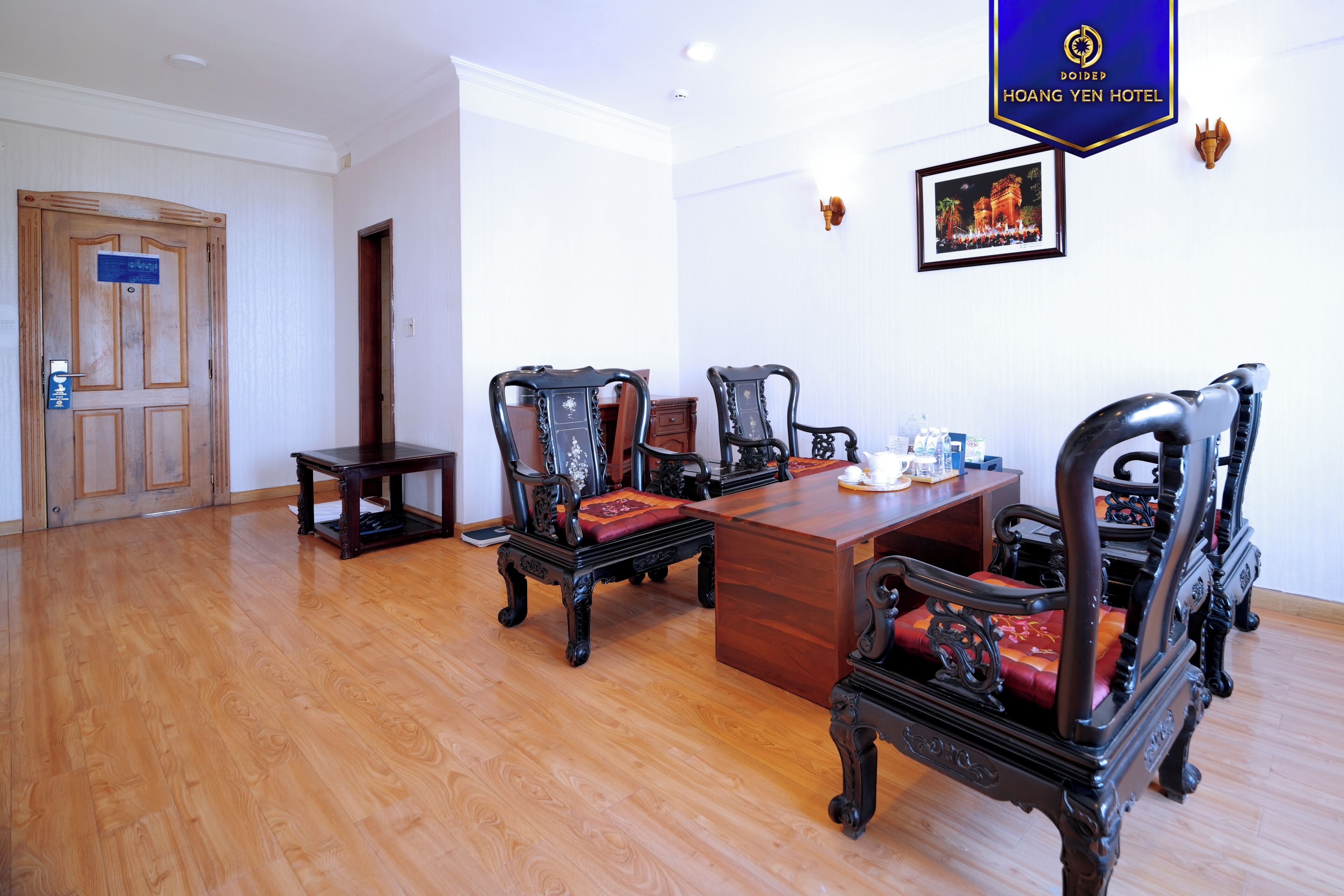 A hotel room with a wooden floor, a wooden desk, and four ornate chairs with red cushions.