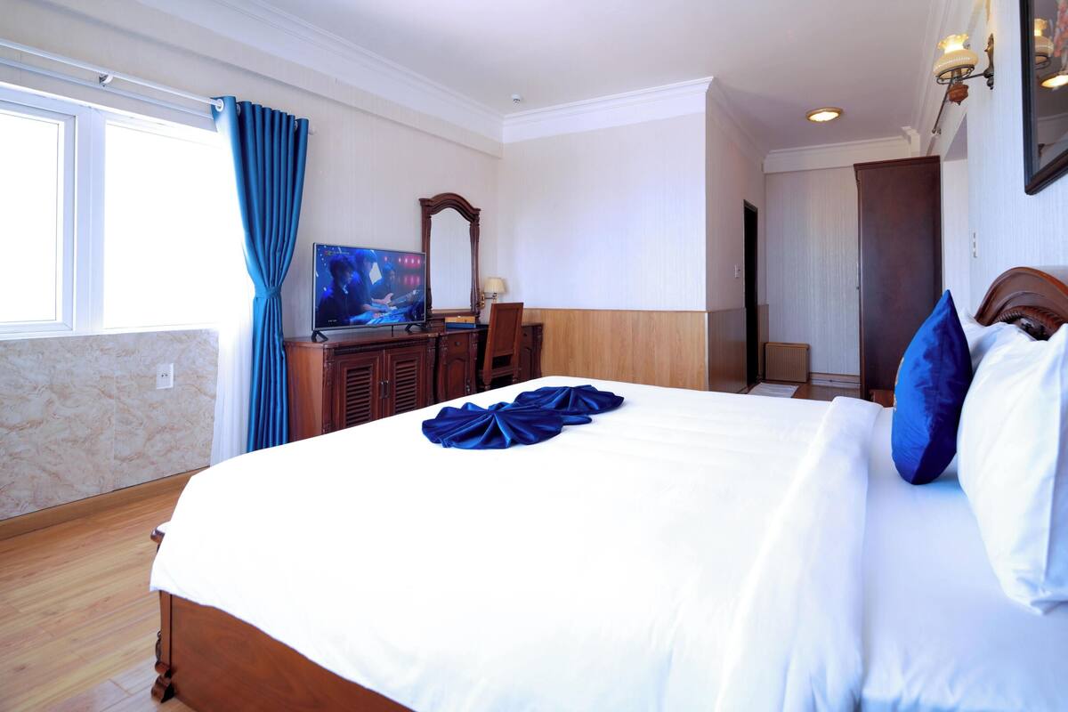 A hotel room with a bed, a television, a desk, and a window with curtains.