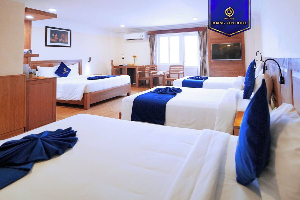 A hotel room with two beds, a desk, a chair, and a TV.