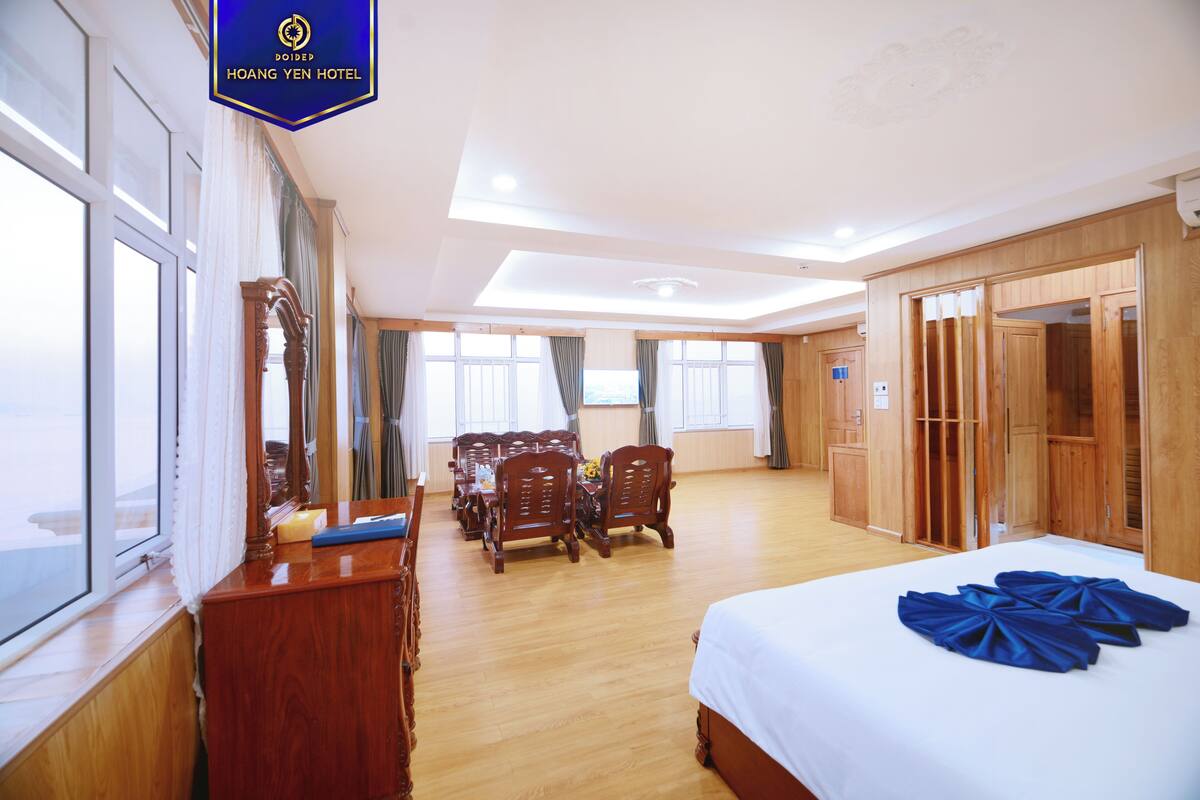 A hotel room with a bed, wooden furniture, a dining table, and a view of the outside.