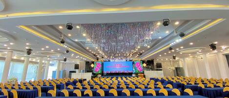 A conference room with rows of chairs, a stage with a large screen, and a ceiling with hanging lights and decorations.