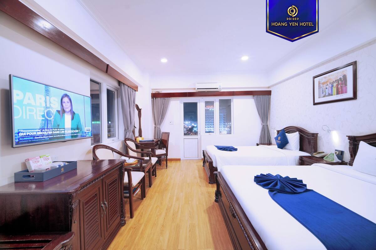 A hotel room with a TV, wooden furniture, a bed with a blue bedspread, and a framed picture on the wall.