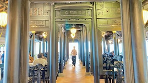 Un couloir orné de colonnes et doté d’une allée centrale, qui mène à une sortie lumineuse.