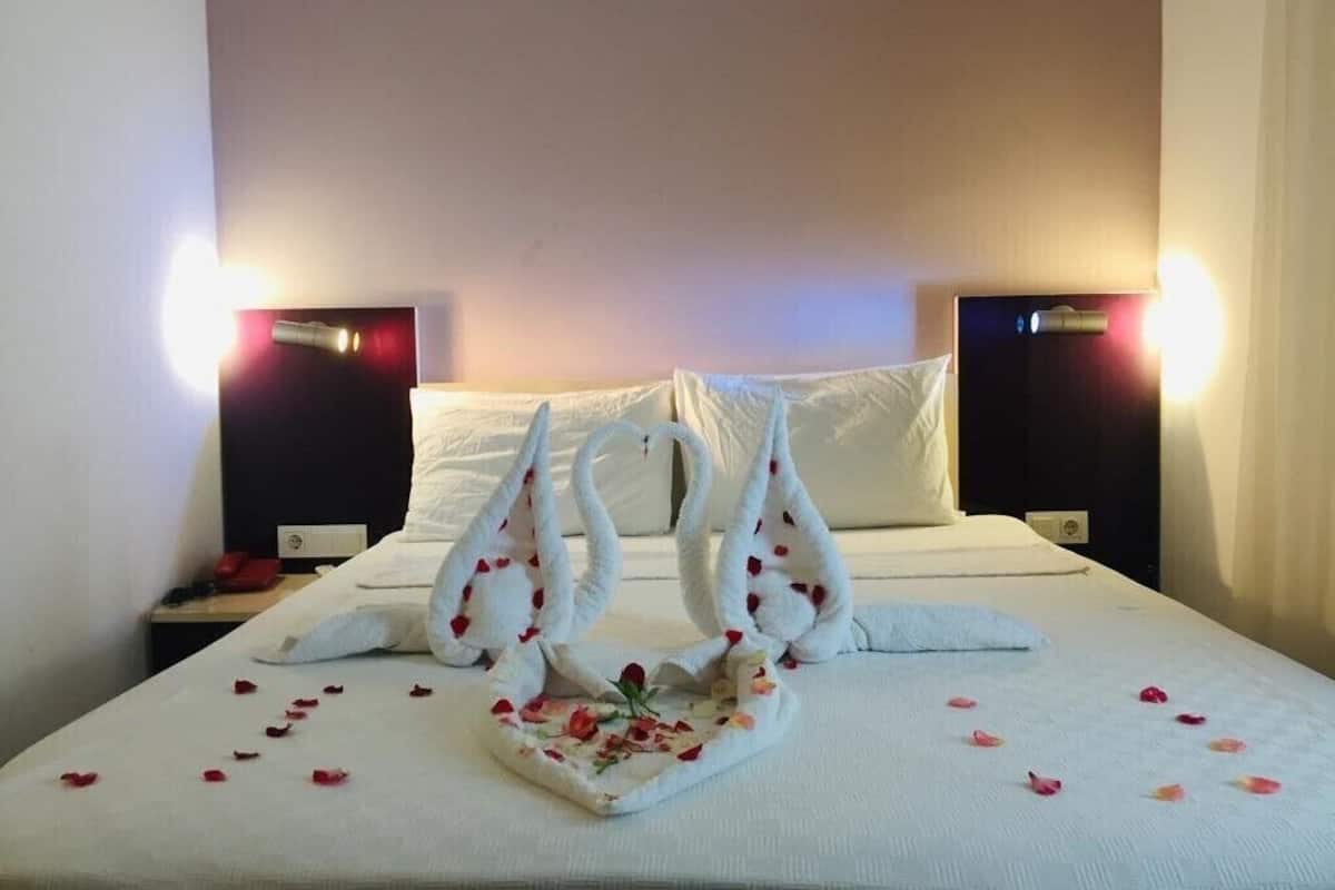 A neatly made bed with a towel arranged in a boat shape, a pillow, and scattered rose petals.