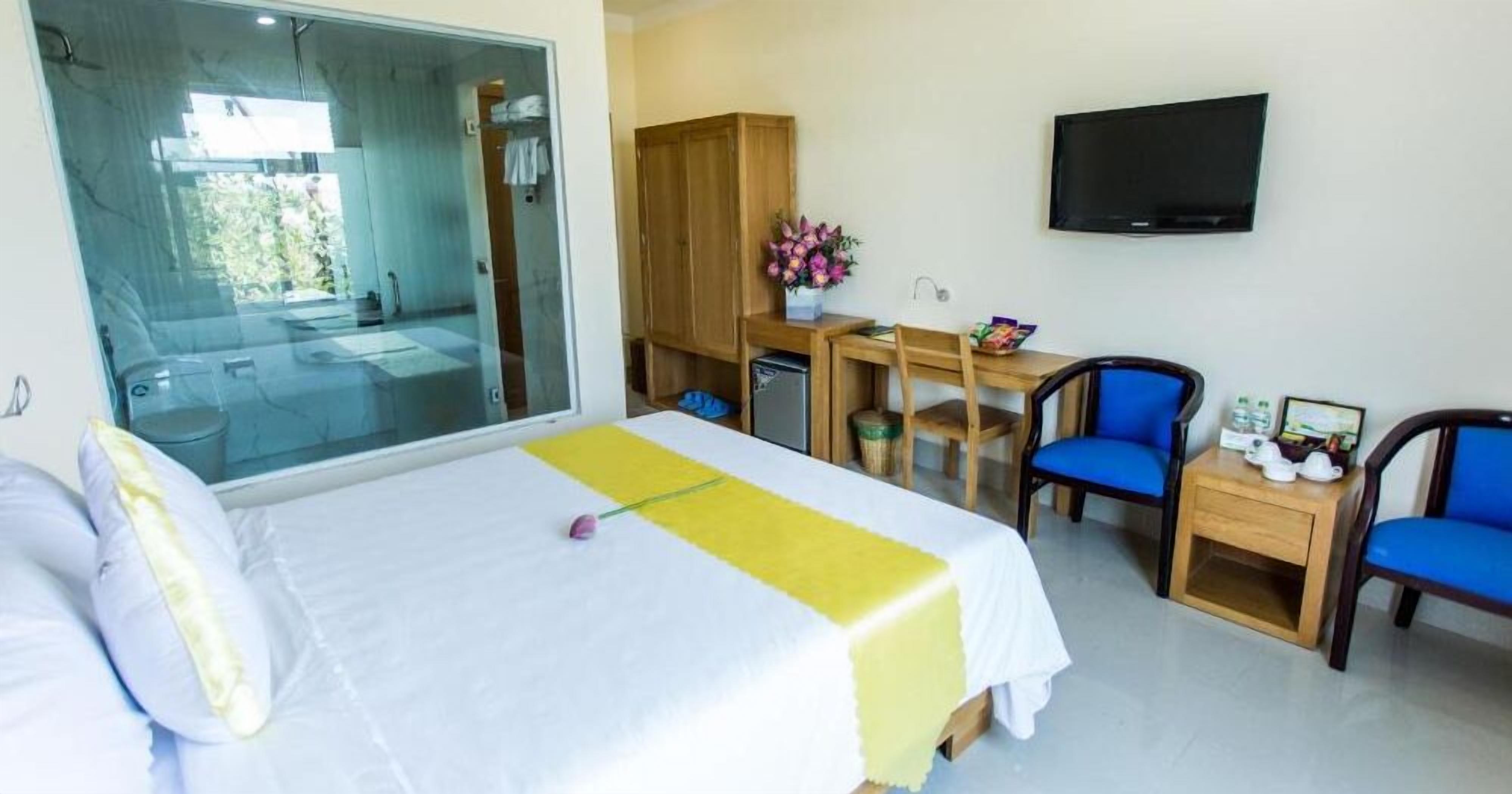 A hotel room with a bed, a desk, two chairs, a TV, and a view through a glass door.