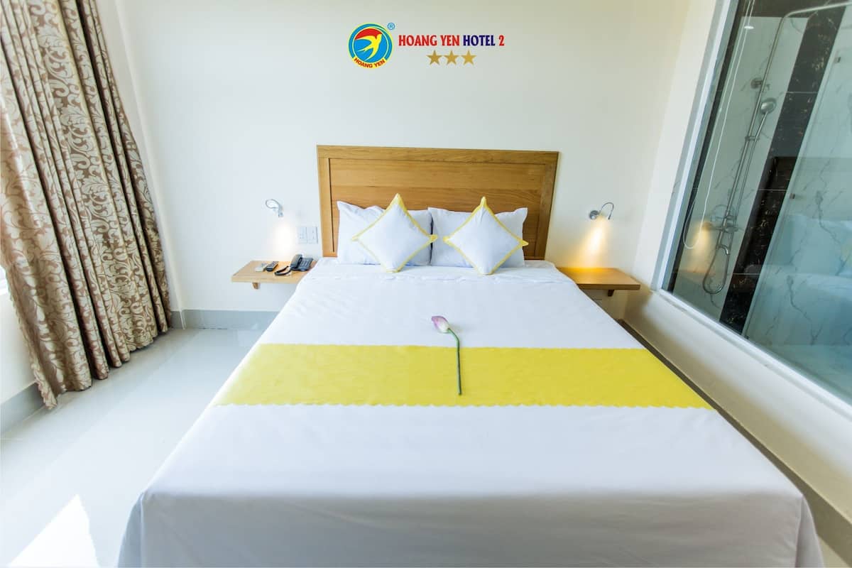 A hotel room with a wooden headboard, white bedding, a yellow accent strip, and a single flower on the bed.