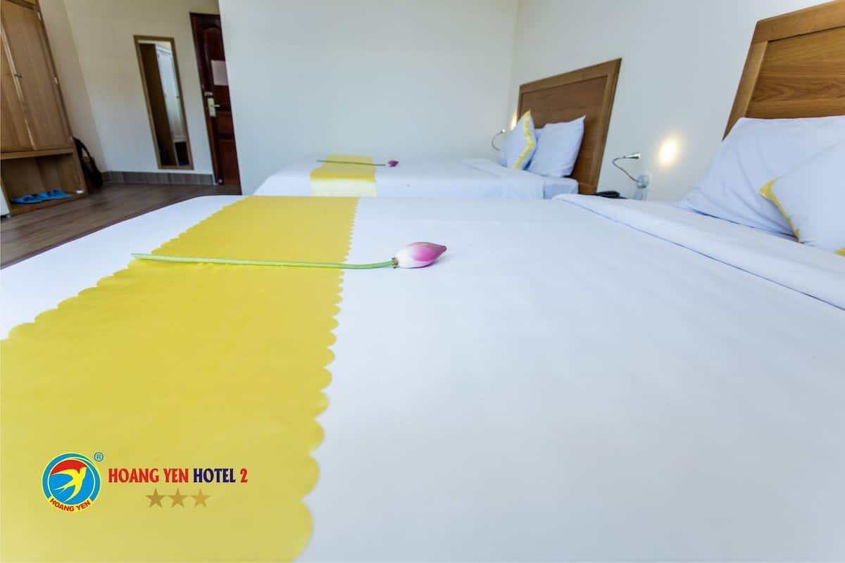 A hotel room with two beds, a wooden headboard, a bedside table with a lamp, and a yellow decorative item on the bed.