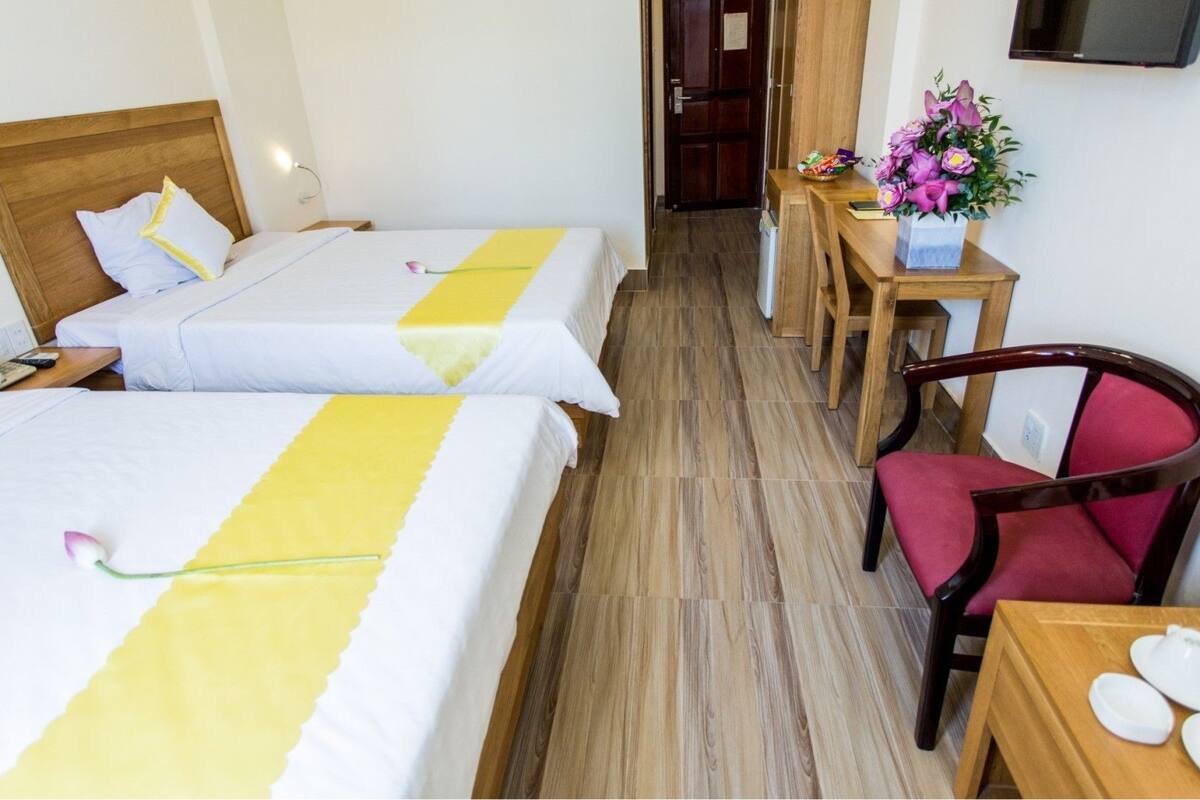 A hotel room with two beds, a wooden nightstand, a desk with a chair, and a television on the wall.