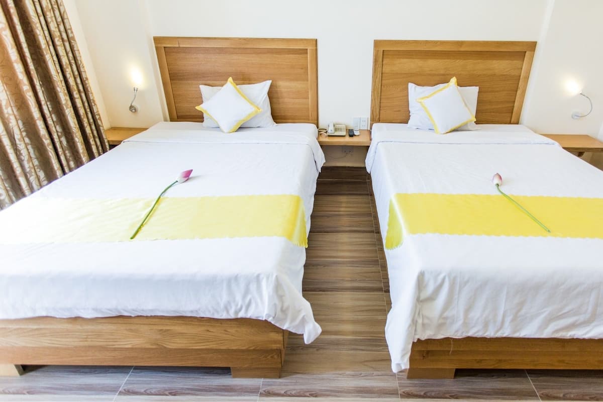 A hotel room with two single beds, wooden headboards, white bedding, and a yellow accent strip.