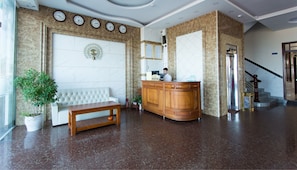 A lobby with a reception desk, a white sofa, a wooden bench, a potted plant, and a staircase. - Hoang Yen 3 Hotel (Quy Nhon)