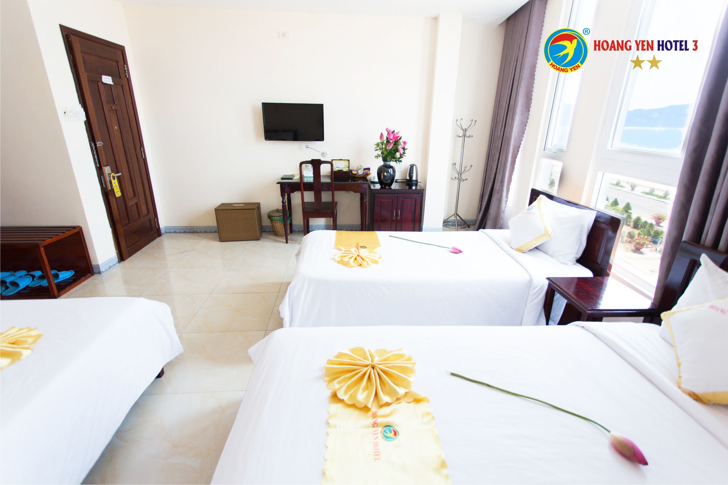 A hotel room with two beds, a desk with a chair, a television, and a window with curtains.