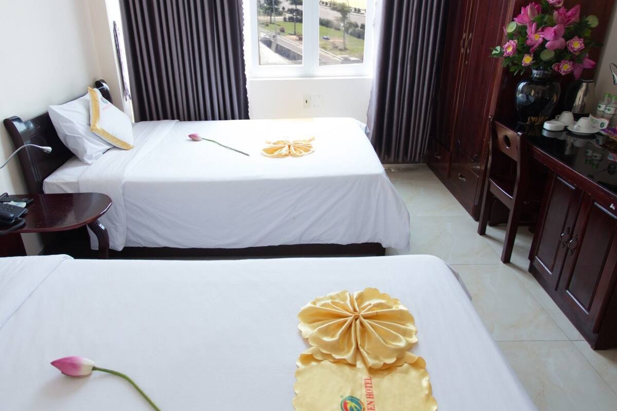 Ein Hotelzimmer mit zwei Betten, einem Schreibtisch mit Computer, einem Telefon und einem Fenster mit Vorhängen.