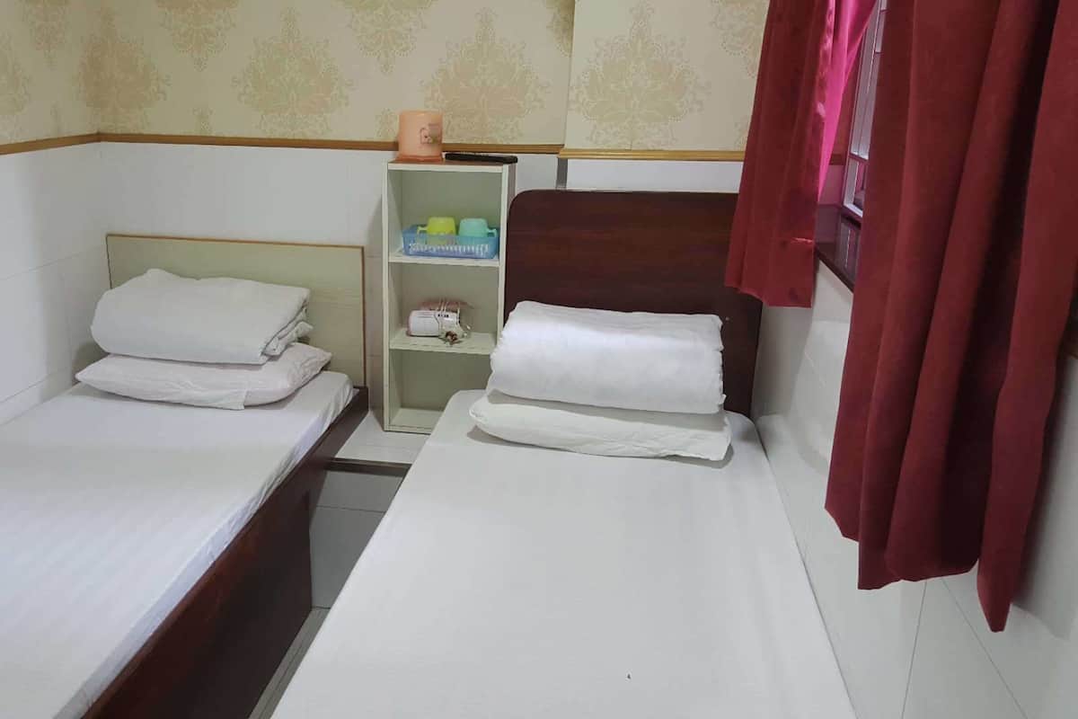 Quarto de hotel pequeno e individual com duas camas, uma prateleira com artigos de higiene pessoal e cortina vermelha.