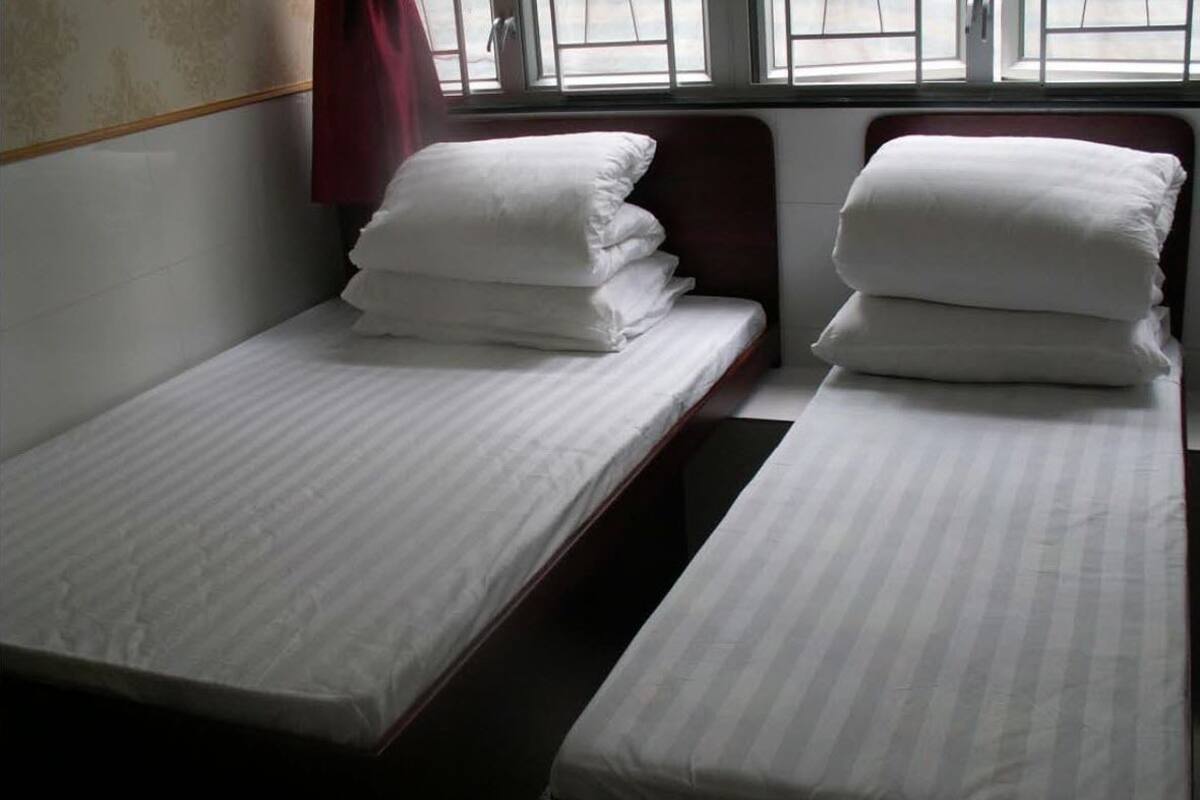 Duas camas de solteiro com roupa de cama e almofadas brancas, um painel de madeira e uma janela com cortinas.