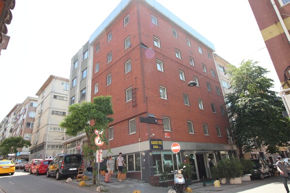 A multi-story building with a red brick facade, a visible entrance, and a sign indicating a hotel.
