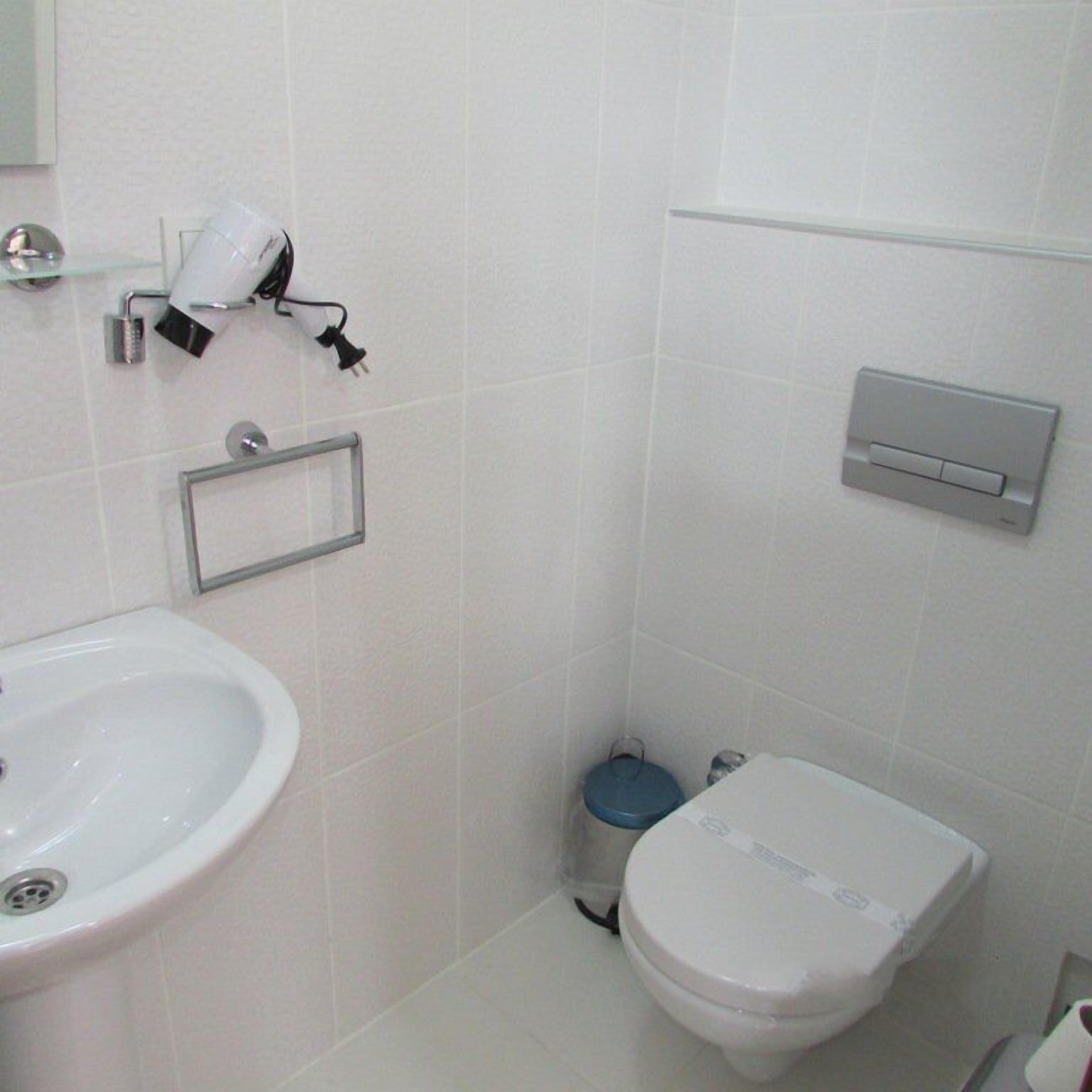 A bathroom with a white sink, toilet, and a small trash bin.