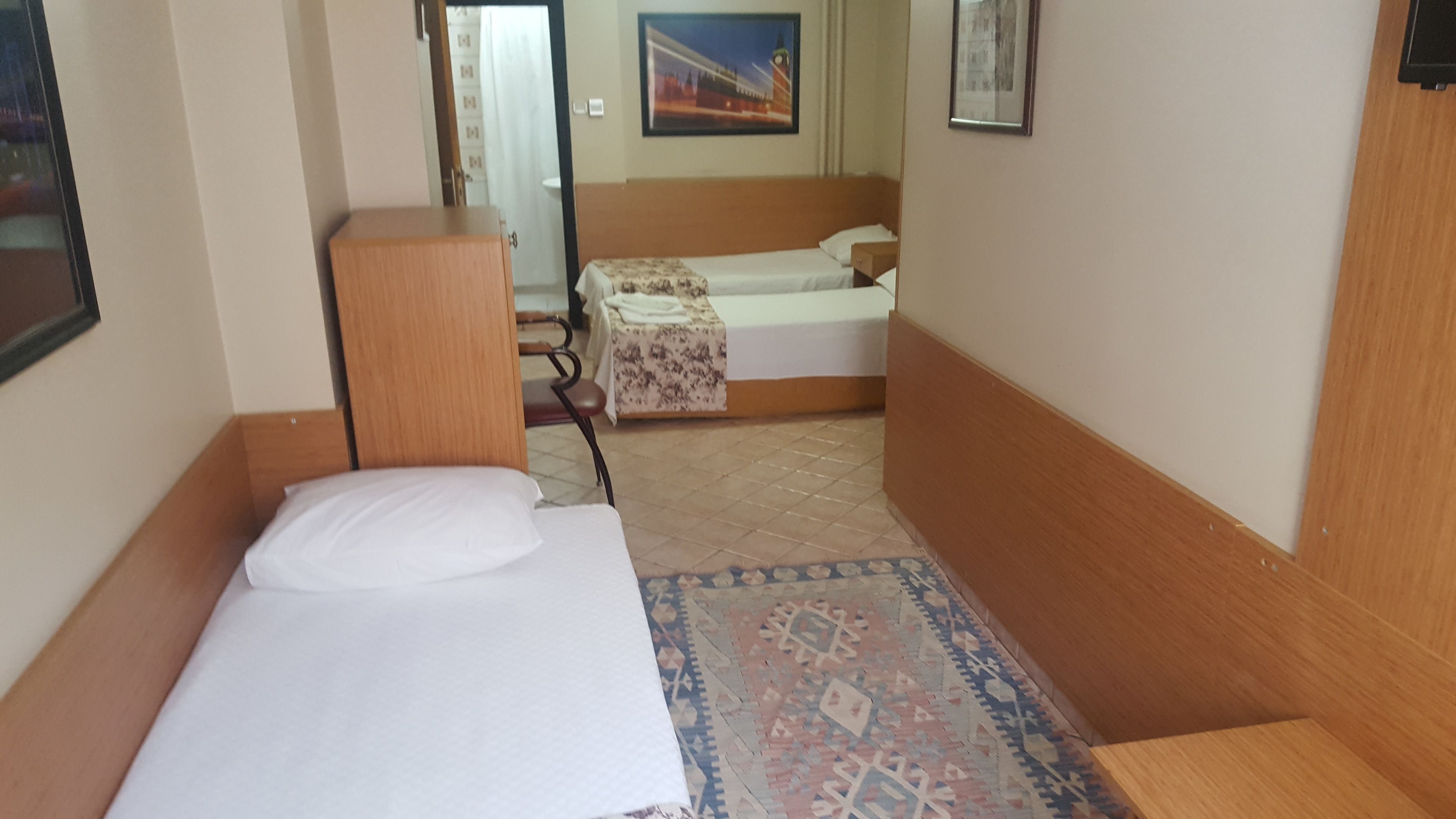 A small, compact room with a single bed, a wooden headboard, and a patterned rug.