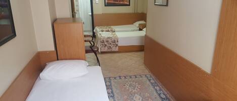 A small, compact room with a single bed, a wooden headboard, and a patterned rug.