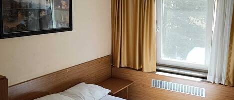 Et hotelværelse med en seng, et vindue med gardiner, en loftsvifte og et billede på væggen.