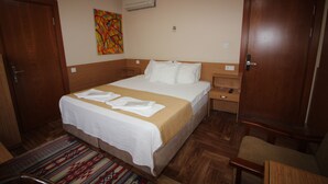 Habitación de hotel con cama, cabecera de madera, mesita de noche, silla, alfombra y un cuadro en la pared.