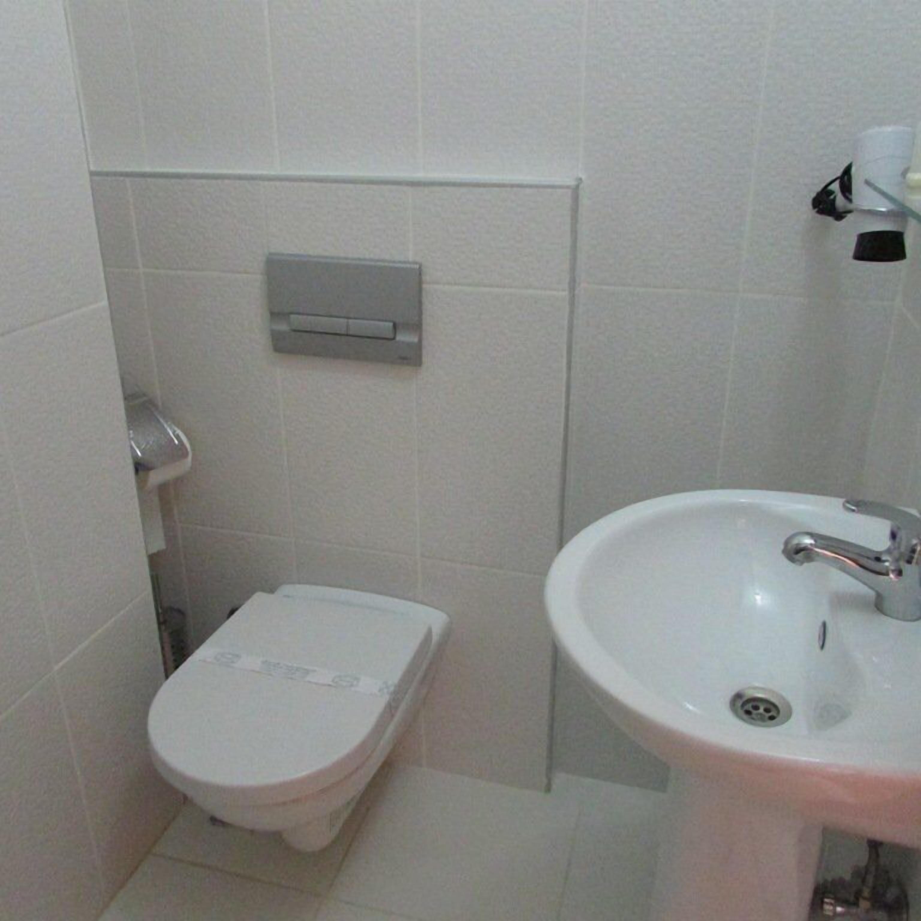 A small bathroom with a toilet, a sink, and a toilet paper holder.