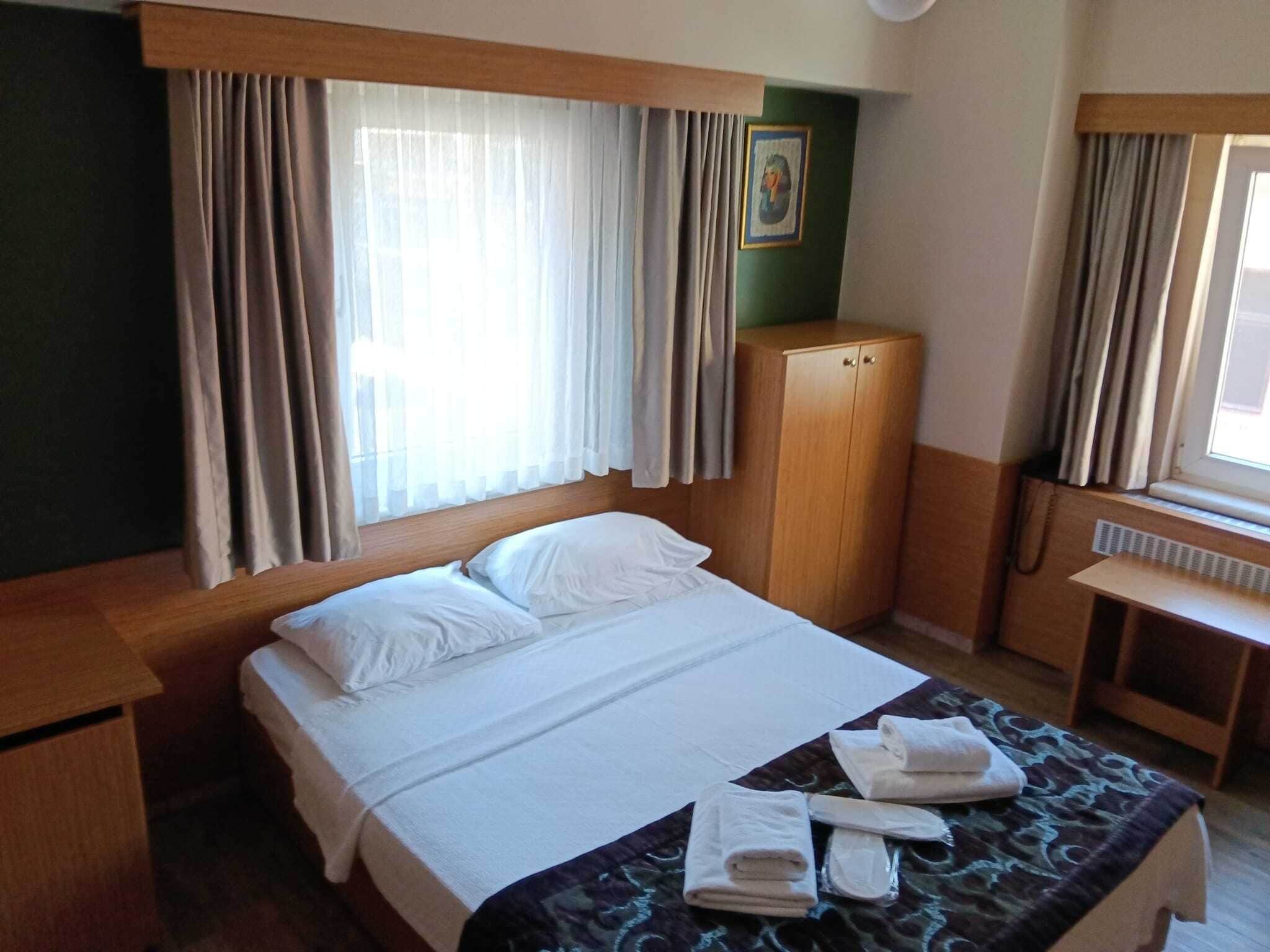 Une chambre d’hôtel avec un lit, un bureau, une armoire et une fenêtre avec des rideaux.