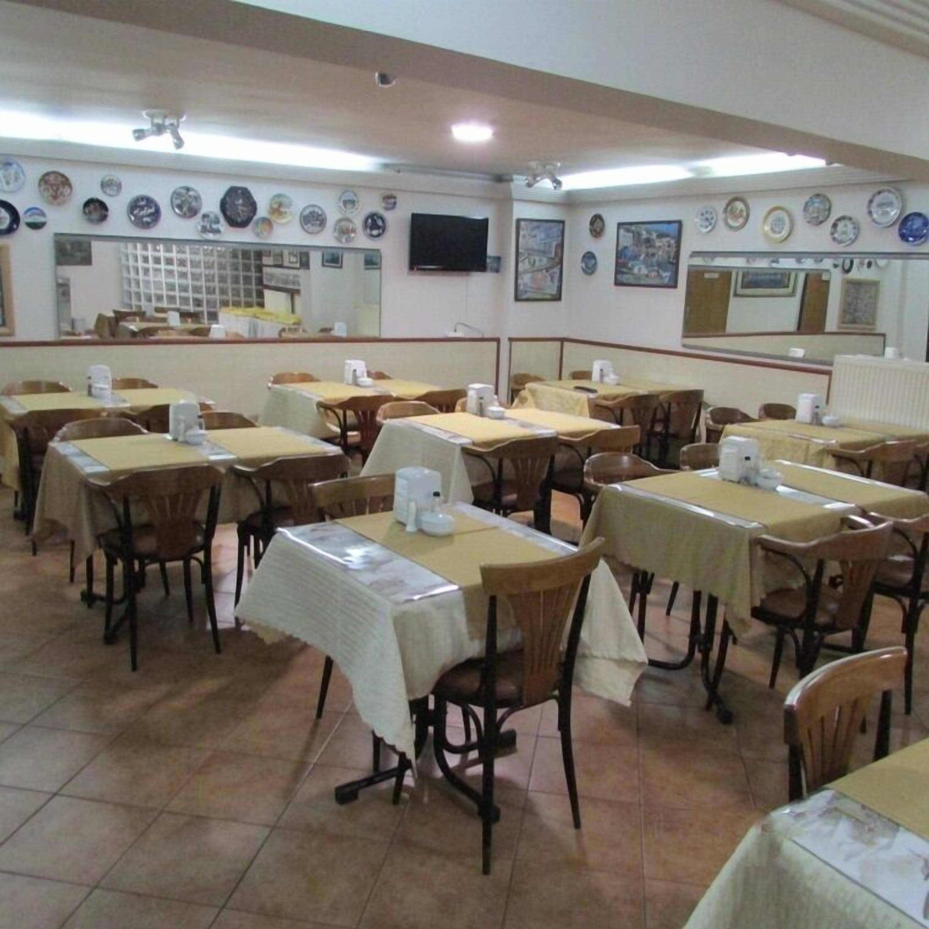 Un comedor con varias mesas y sillas, piso de baldosas y decoración en las paredes que incluye platos y cuadros.