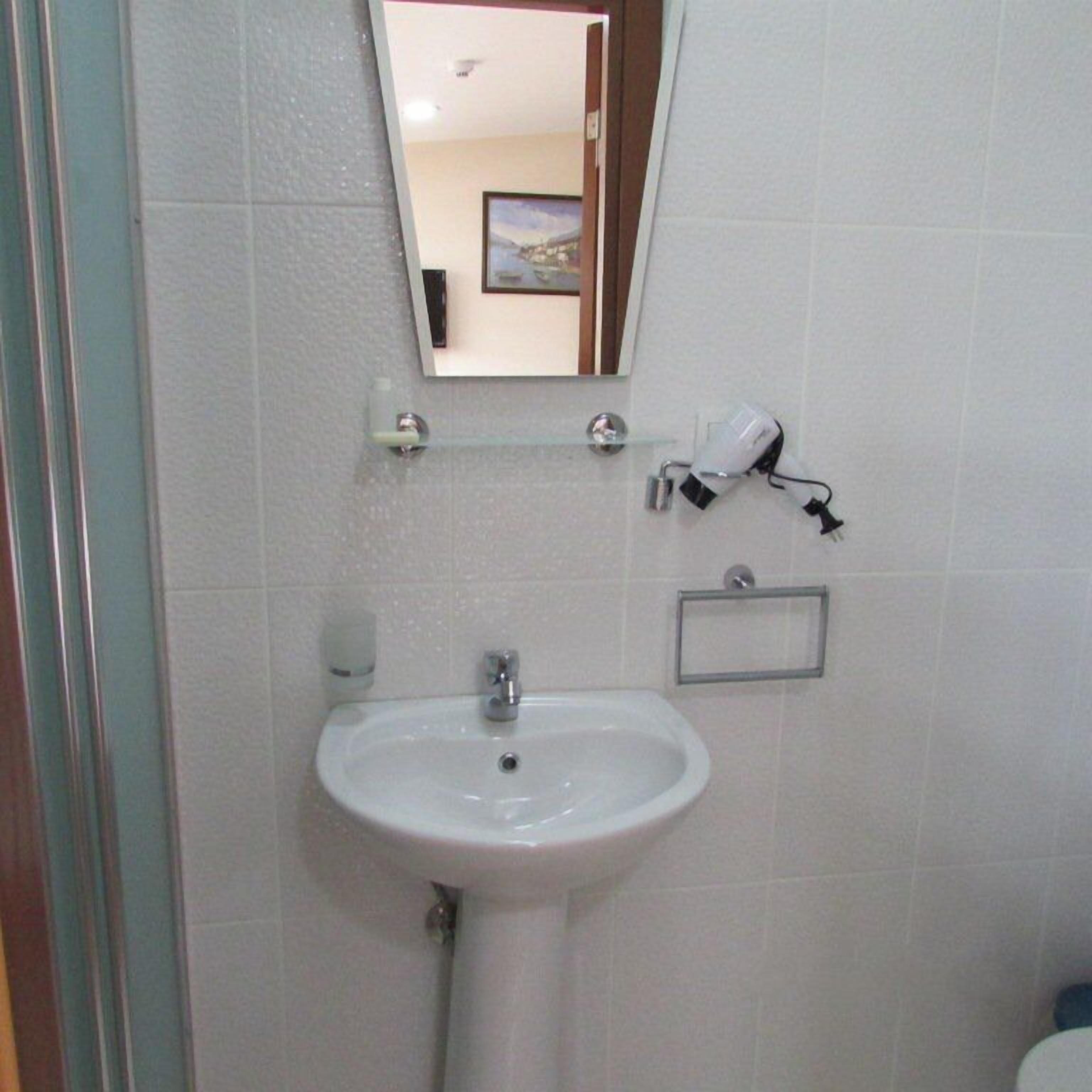 Ein Badezimmer mit einem weißen Waschbecken, einem Spiegel und einem Föhn an der Wand.