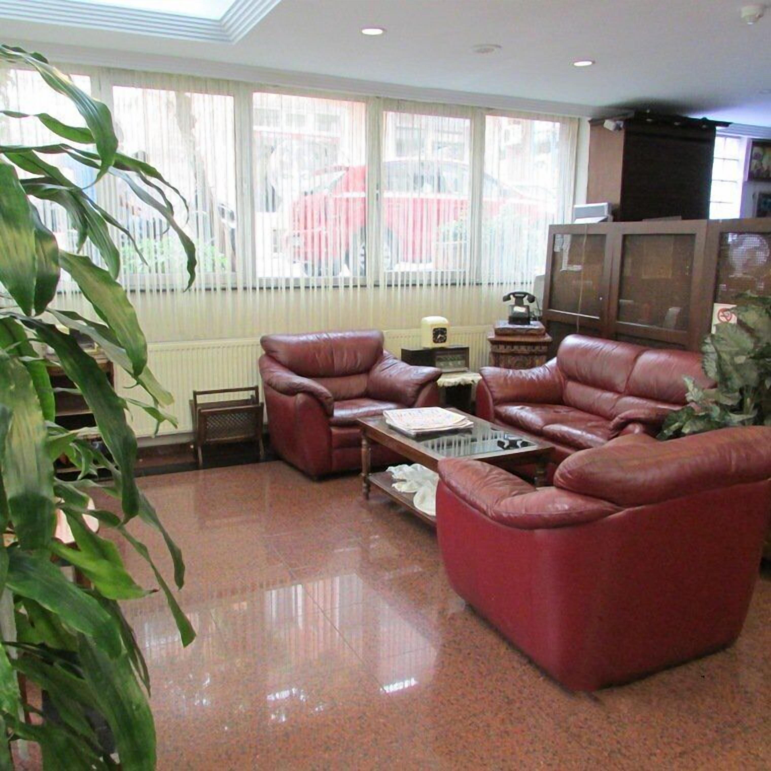 A living room with a red leather sofa, a glass coffee table, and a large window with blinds.
