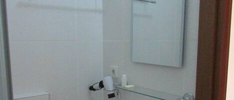 Un baño pequeño con un lavamanos blanco, un espejo y un estante de vidrio.