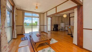 A traditional Japanese-style room with tatami mats, a wooden table, and a sliding door leading to a balcony with a view of the sea. - Pension Coral (Nakijin)