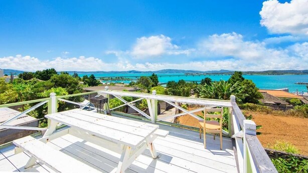 A wooden deck with a bench and chair overlooking a beach with clear turquoise waters and distant mountains. - Pension Coral (Nakijin)