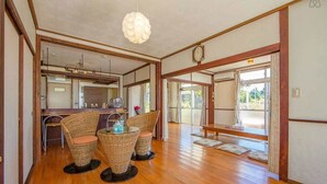 A traditional Japanese-style room with a wooden floor, a dining area with wicker chairs, a hanging light fixture, and a view through a sliding door. - Pension Coral (Nakijin)