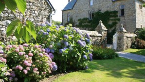 A stone building with a traditional design, featuring a well-maintained garden with hydrangea bushes. - Le Manoir de la Fieffe (Cherbourg-en-Cotentin)