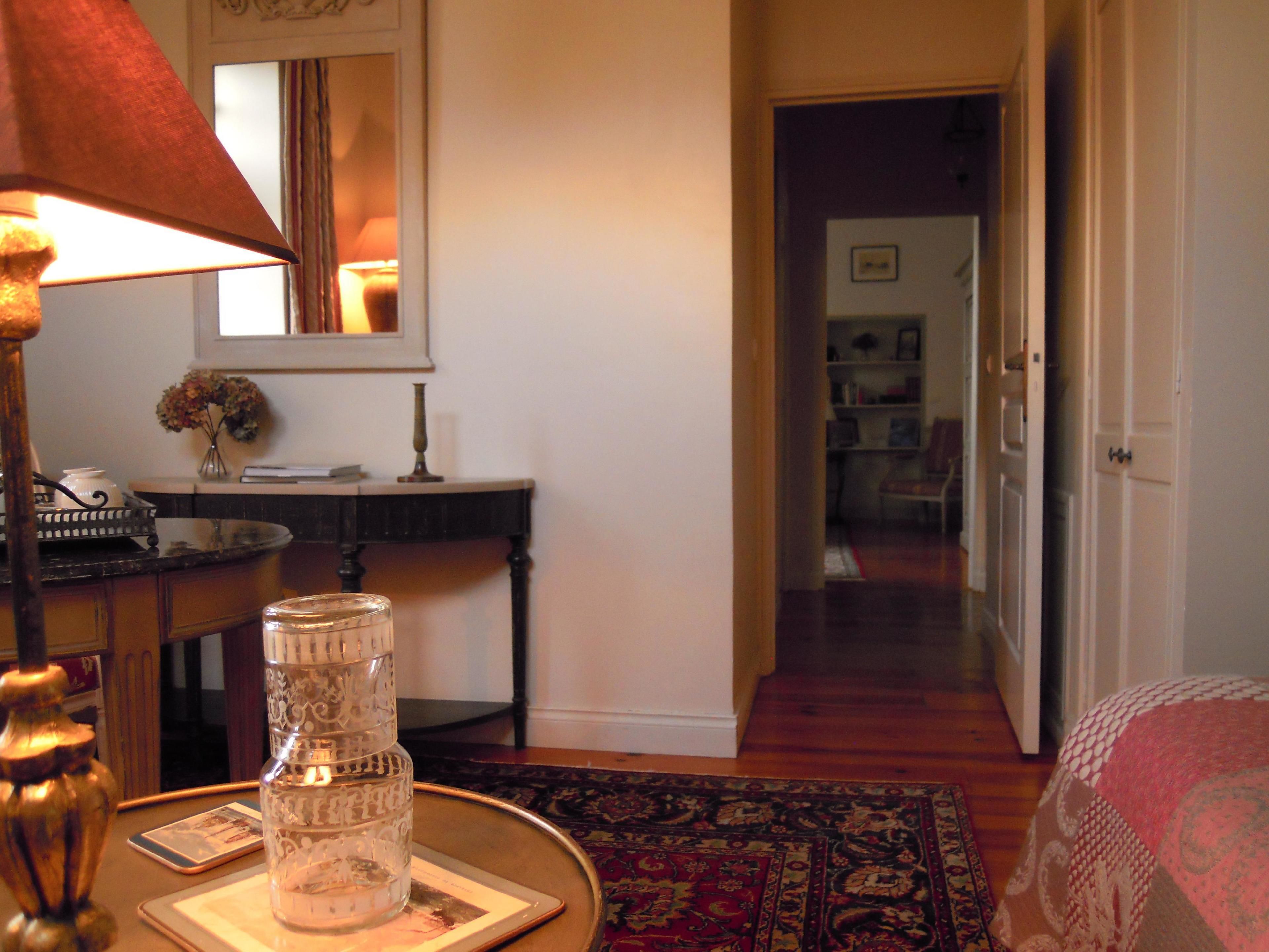 A cozy room with a wooden desk, a lamp, a vase with flowers, and a bookshelf in the background.