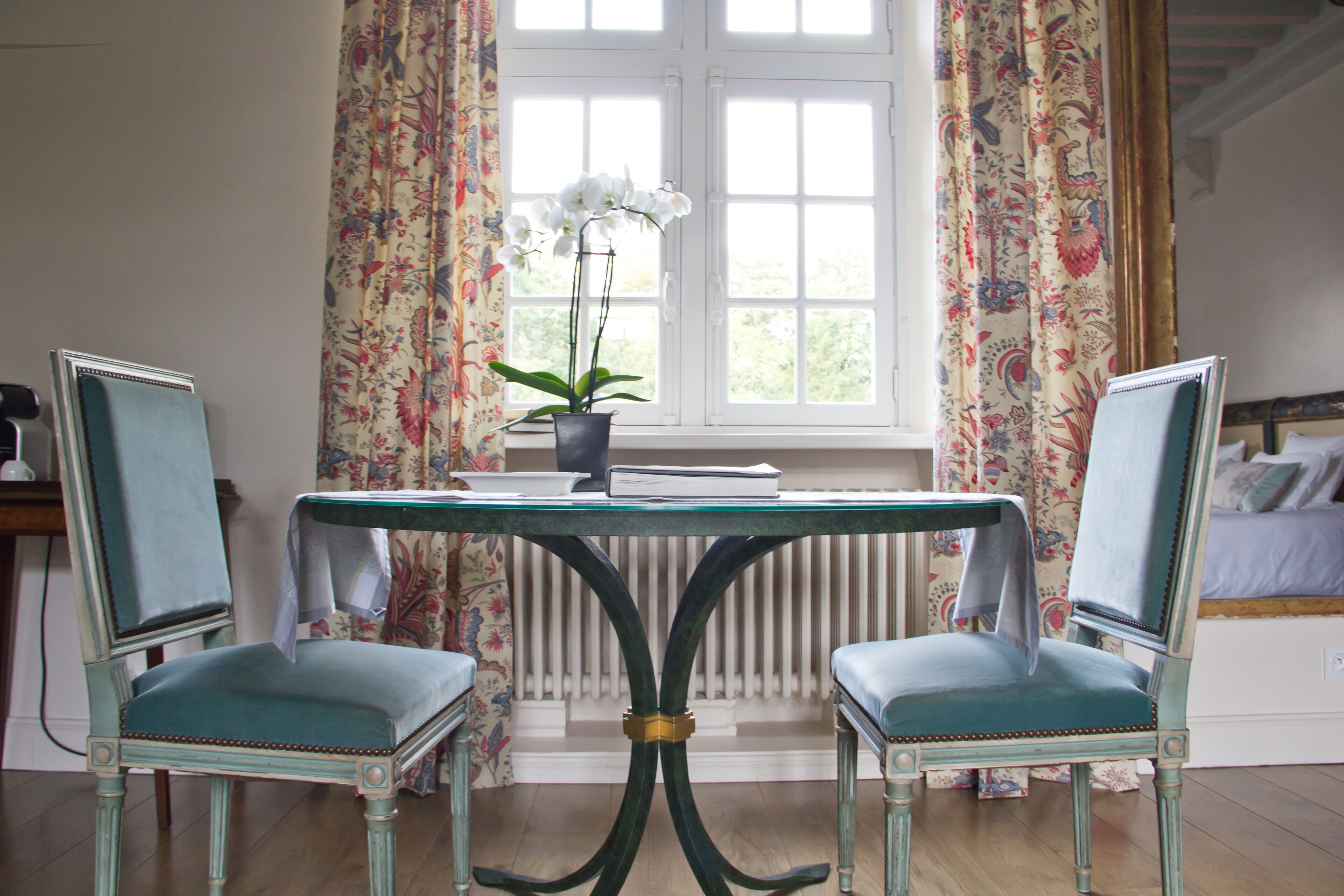 A room with a table and two chairs, a potted plant, and a window with curtains.