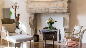 A room with a fireplace, a wicker sofa, a striped chair, and a table with a vase of flowers. - Le Manoir de la Fieffe (Cherbourg-en-Cotentin)