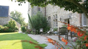 A stone building with a paved patio, outdoor seating, and lush greenery. - Le Manoir de la Fieffe (Cherbourg-en-Cotentin)