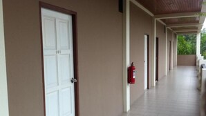 A corridor with a white door marked 105, a red fire extinguisher, and a covered walkway with a tiled floor. - Baan Chomphu (Prachuap Khiri Khan)