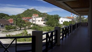 A covered balcony with a view of a hilltop building and surrounding greenery. - Baan Chomphu (Prachuap Khiri Khan)