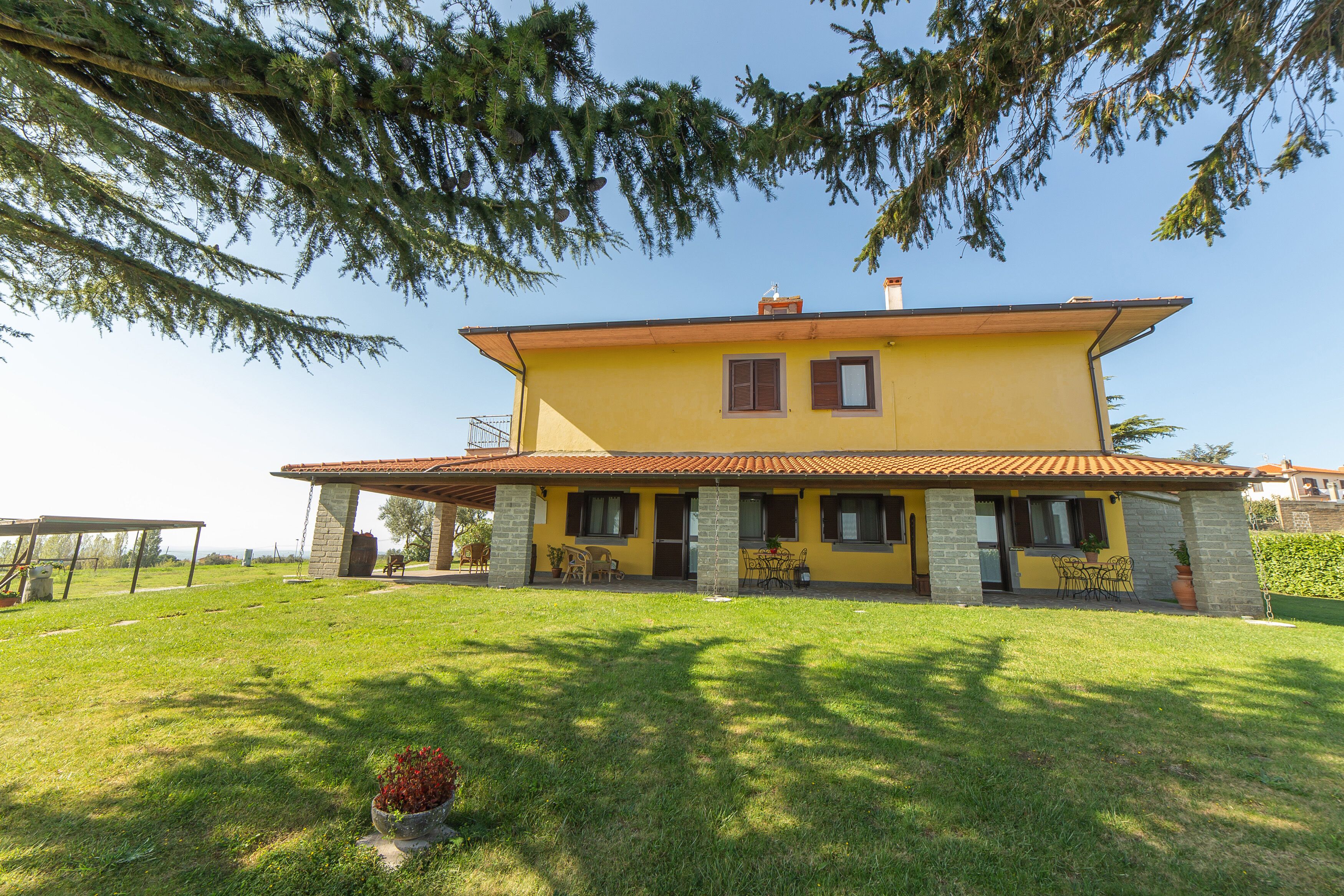 Une maison à deux étages avec une façade jaune, des piliers en pierre et un toit recouvert de tuiles.