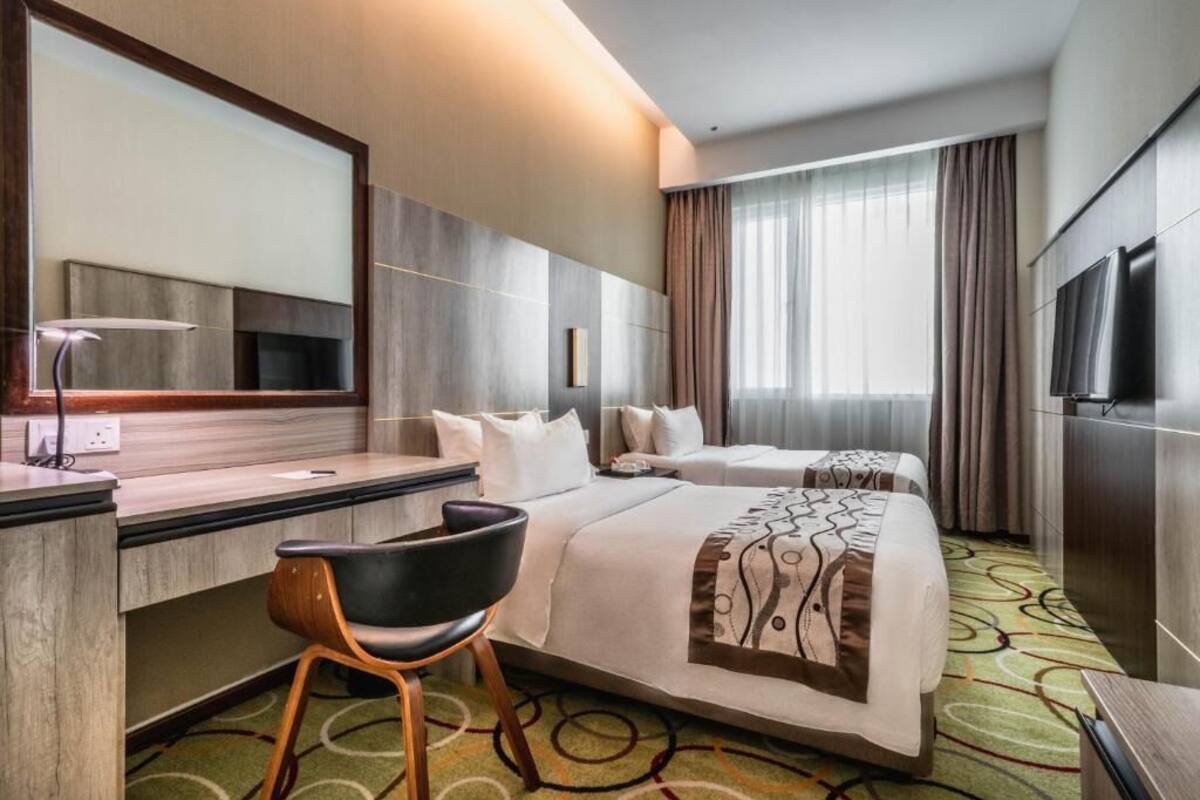 Una habitación de hotel con una cama grande, un escritorio con silla, un televisor y un espejo amplio.